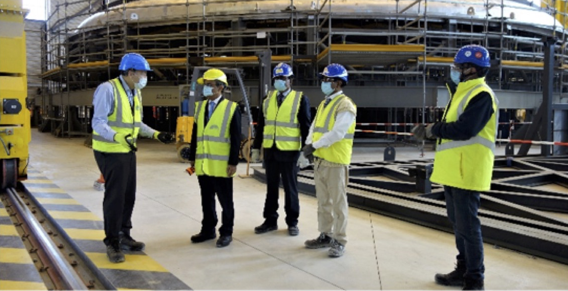 r. Bigot explaining the construction progress to the visitors in the back drop of the cryostat top lid section at ITER site. 